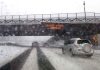 Cars driving in snow under winter storm warning sign