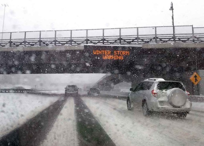 Cars driving in snow under winter storm warning sign