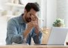 Man holding glasses, looking tired at laptop.