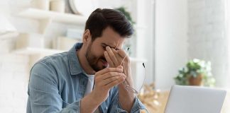 Man holding glasses, looking tired at laptop.