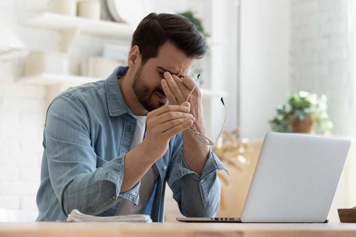 Man holding glasses, looking tired at laptop.