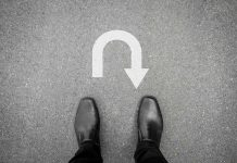 Feet in black shoes facing U-turn road marking.