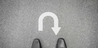 Feet in black shoes facing U-turn road marking.