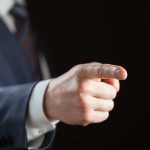 Person pointing with finger, wearing a suit.