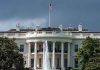 White House with American flag and fountain, stormy sky.