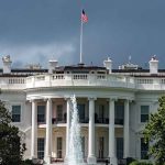 White House with American flag and fountain, stormy sky.