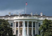 White House with American flag and fountain, stormy sky.