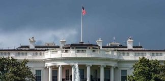 White House with American flag and fountain, stormy sky.