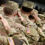 Soldiers in camouflage uniforms saluting in formation outdoors