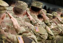 Soldiers in camouflage uniforms saluting in formation outdoors