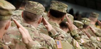 Soldiers in camouflage uniforms saluting in formation outdoors