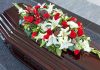 Casket with red, white lily, and gerbera flower arrangement.