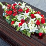 Casket with red, white lily, and gerbera flower arrangement.