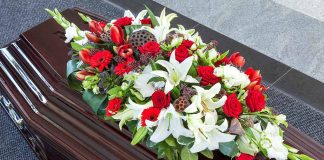 Casket with red, white lily, and gerbera flower arrangement.