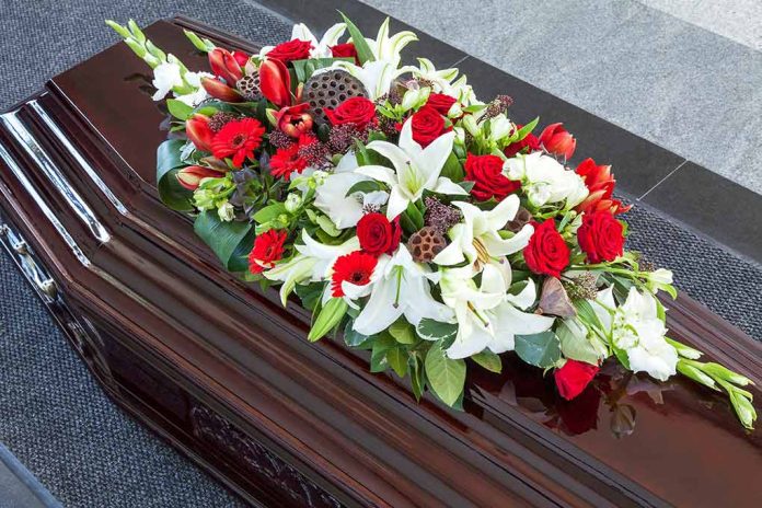 Casket with red, white lily, and gerbera flower arrangement.