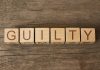 Wooden blocks spell out "GUILTY" on wood background.