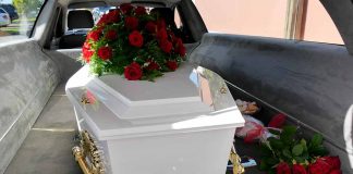 White coffin with red roses inside a hearse.