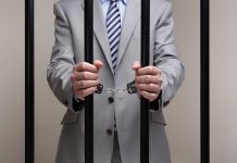 Person in suit handcuffed behind jail bars.