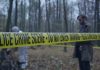 Police crime scene tape in forest with investigators