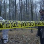 Police crime scene tape in forest with investigators