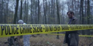 Police crime scene tape in forest with investigators