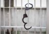 Open handcuff hanging on white prison bars