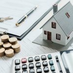 House model, coins, pen, and calculator on documents.