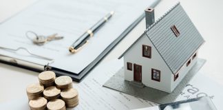 House model, coins, pen, and calculator on documents.