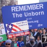 Pro-life marchers holding various anti-abortion signs.
