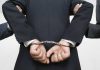 Person handcuffed in suit escorted by two others
