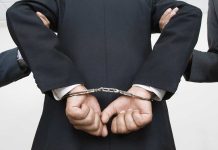 Person handcuffed in suit escorted by two others