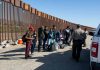 Group of people at border wall with patrol agents.