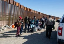 Group of people at border wall with patrol agents.