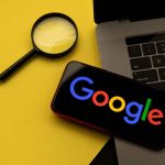 Magnifying glass laptop and smartphone displaying Google s logo