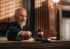 Judge holding gavel in a courtroom setting.