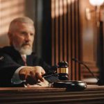 Judge holding gavel in a courtroom setting.