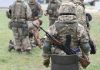 Soldiers in camouflage gear gathered on grass field