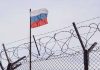Barbed wire fence with Russian flag in background.