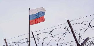 Barbed wire fence with Russian flag in background.