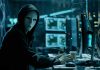 Person wearing mask and hoodie at computer desk