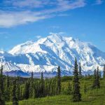 Snow covered mountain under blue sky with green foreground