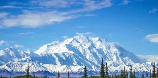 Snow covered mountain under blue sky with green foreground
