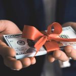 Hands holding stack of hundreddollar bills with ribbon