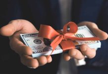 Hands holding stack of hundreddollar bills with ribbon