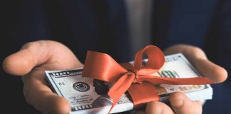Hands holding stack of hundreddollar bills with ribbon