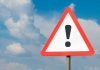 Warning sign with exclamation mark against cloudy sky
