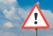 Warning sign with exclamation mark against cloudy sky