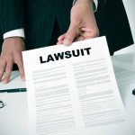 Person holding a document titled LAWSUIT in office