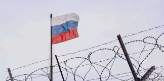 Barbed wire fence with Russian flag in background