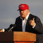 Person speaking at a podium wearing a red hat